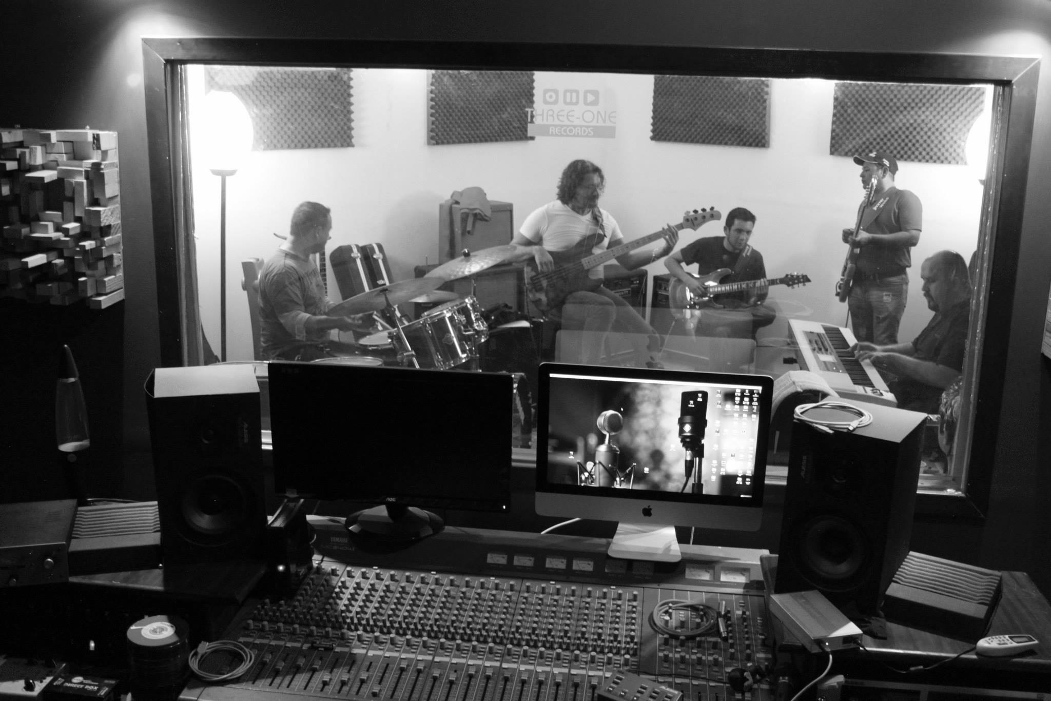 Vista en blanco y negro desde el control mientras Guillermo graba guitarra con un ensamble.